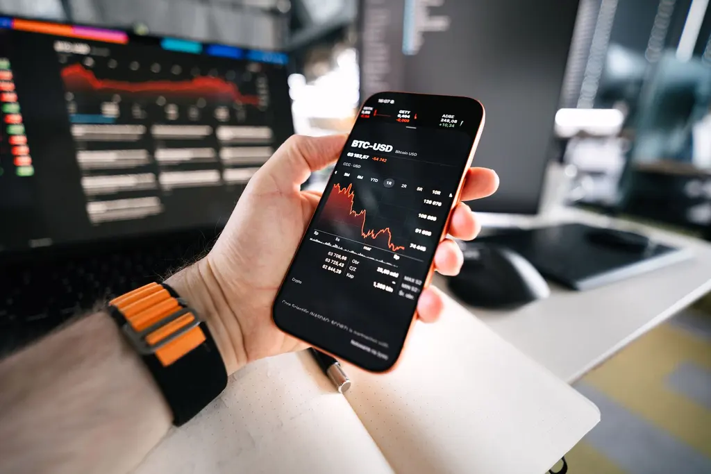 Mão segurando um celular com o gráfico de preço BTC-USD